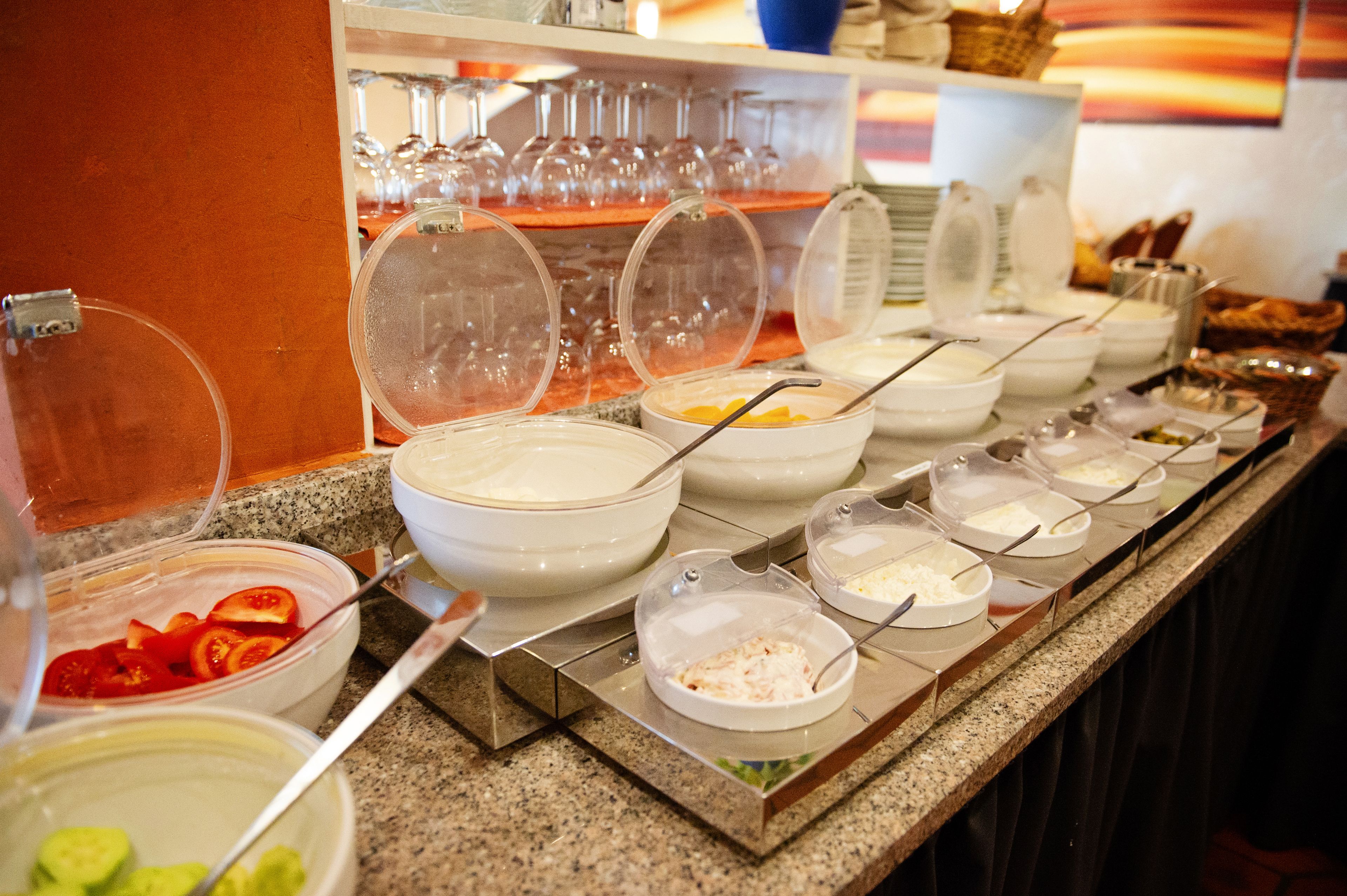 A buffet line with various food items and a glassware section in the background.