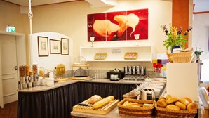 A buffet setup with various food items and beverages, a coffee station, and a decorative wall with framed pictures and a large floral artwork. - Hotel Heideparadies (Soltau)