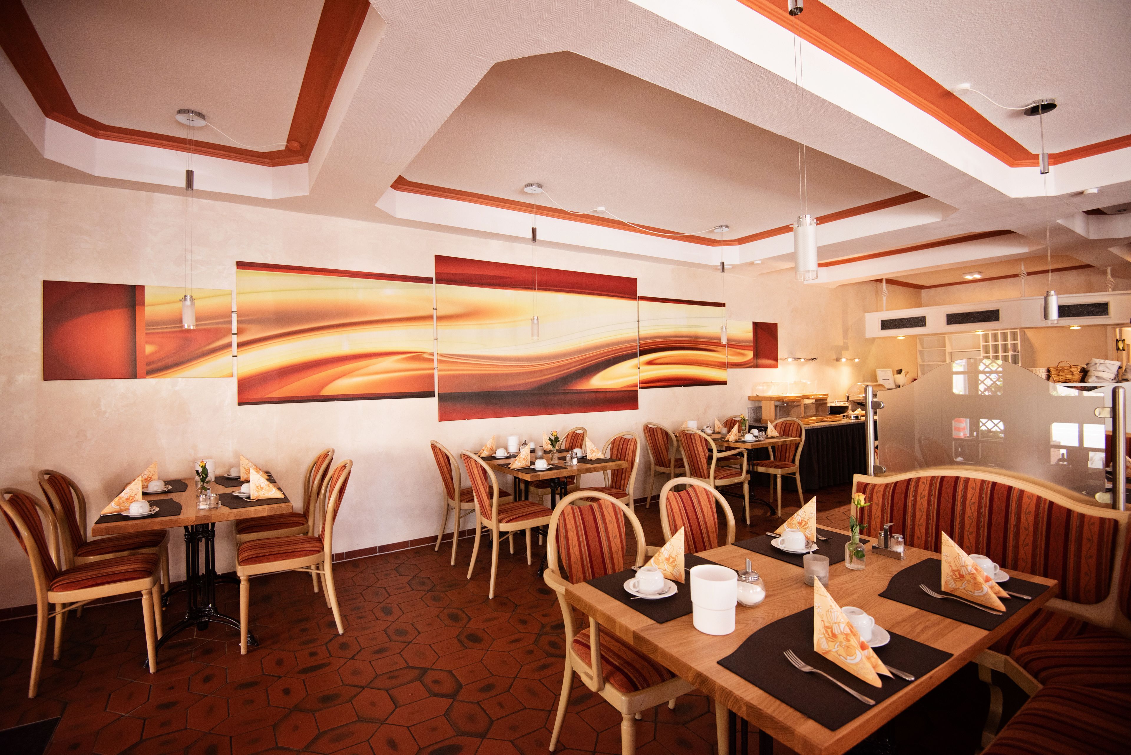 Un restaurante con mesas y sillas de madera, un gran arte mural abstracto y un suelo con estampado hexagonal.