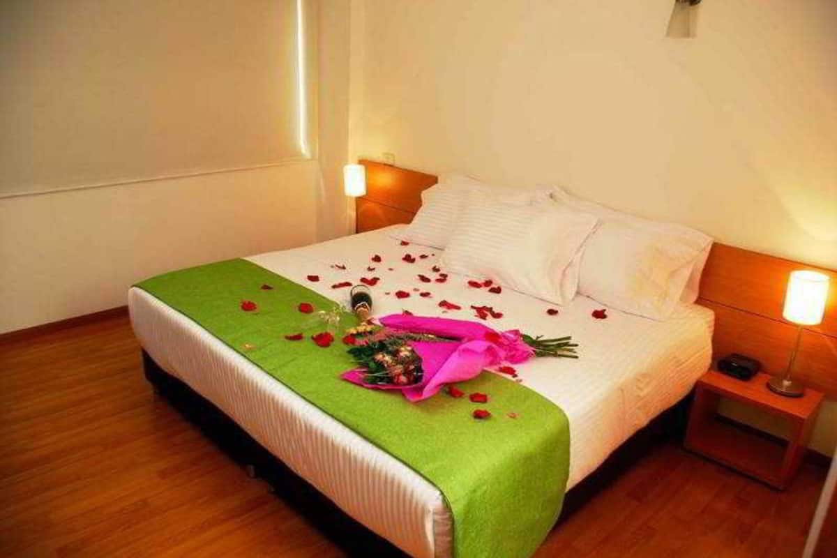 Ein ordentlich bezogenes Bett mit einer grünen Tagesdecke, weißen Kissen und Rosenblüten, die auf dem Bett verteilt sind.