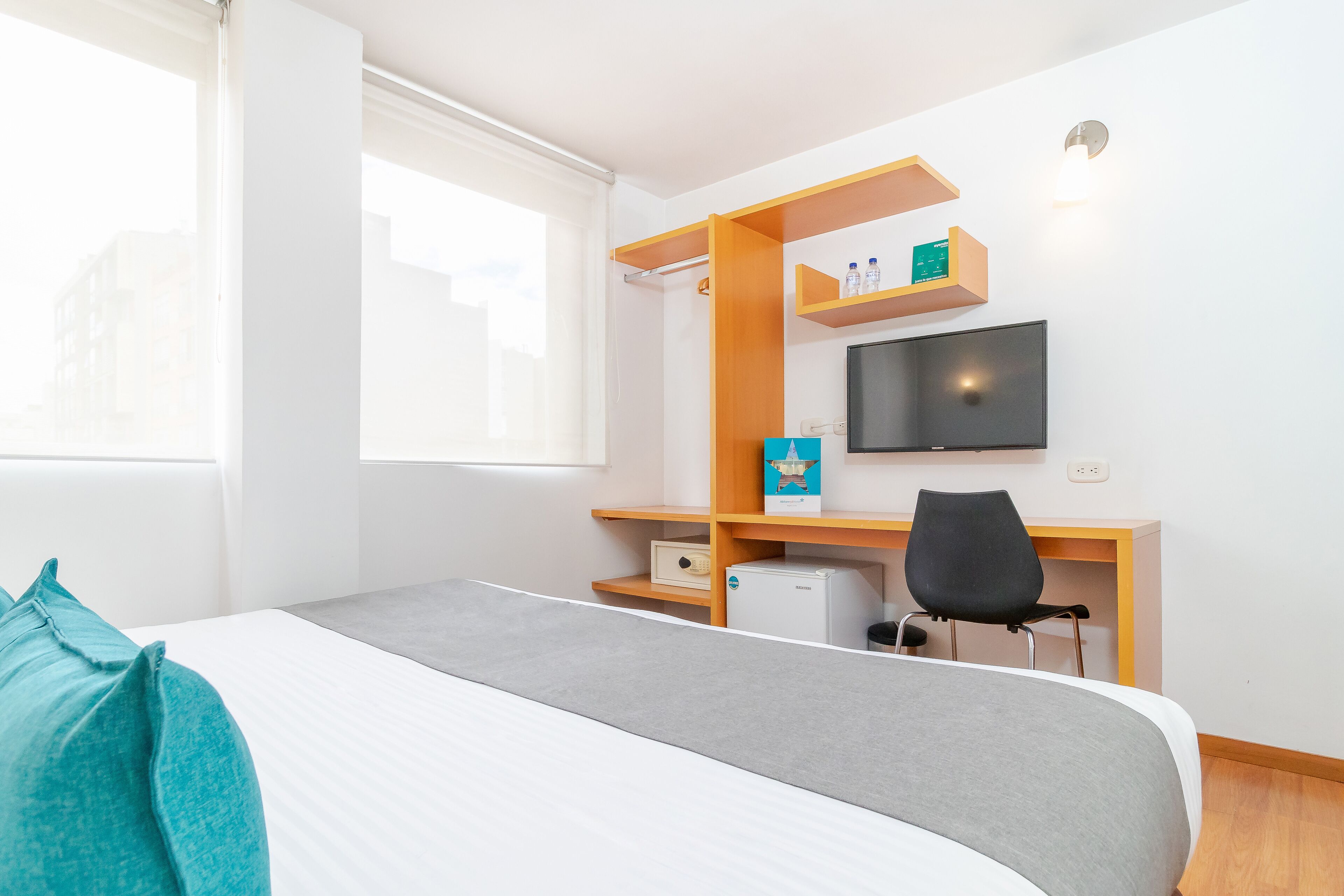Een hotelkamer met een bed, een bureau met stoel, een televisie en een raam.