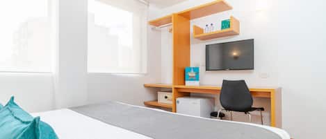 A hotel room with a bed, a desk with a chair, a television, and a window.