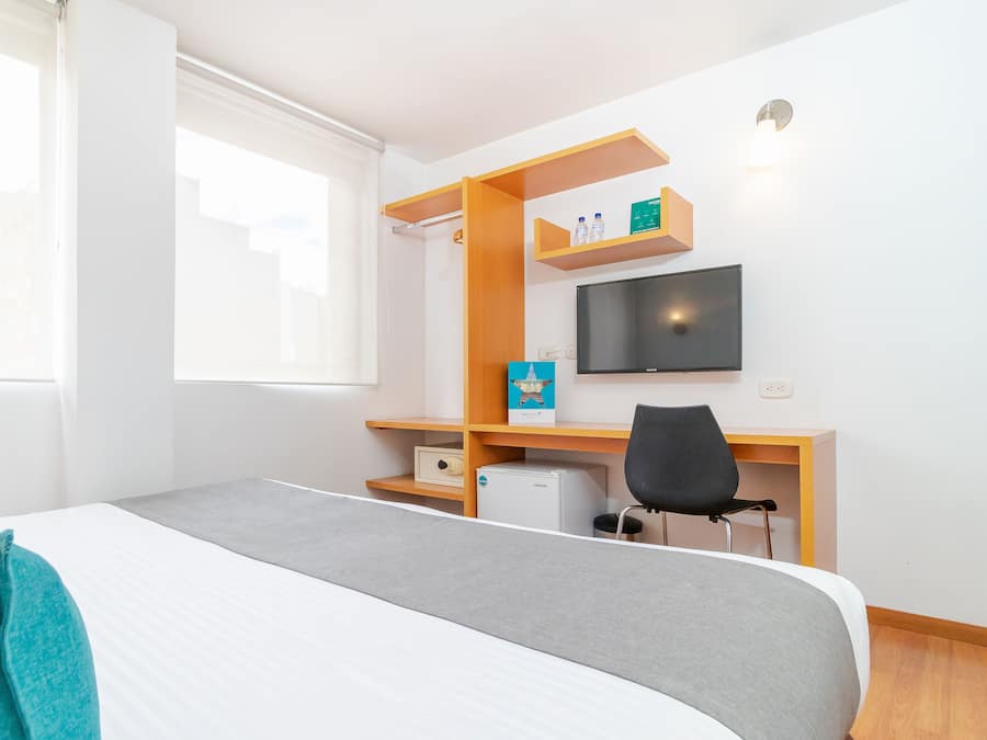 A hotel room with a bed, a desk with a chair, a television, and a window.