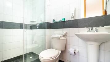 A modern bathroom with a glass shower enclosure, a white toilet, a sink with a mirror, and a towel rack.