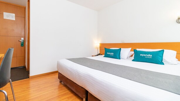 Habitación de hotel con cama, mesita de noche, una silla y una puerta de madera.