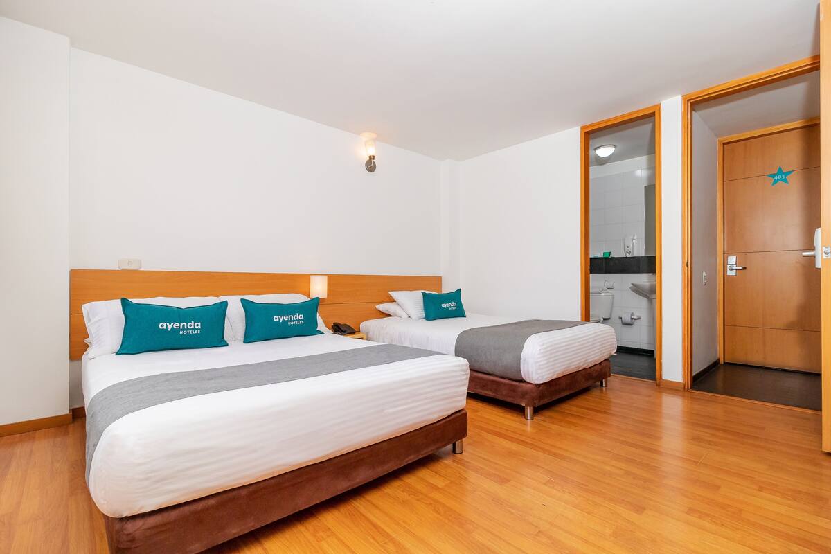 A hotel room with two beds, wooden flooring, a bathroom visible through an open door, and a star rating sign on the door.