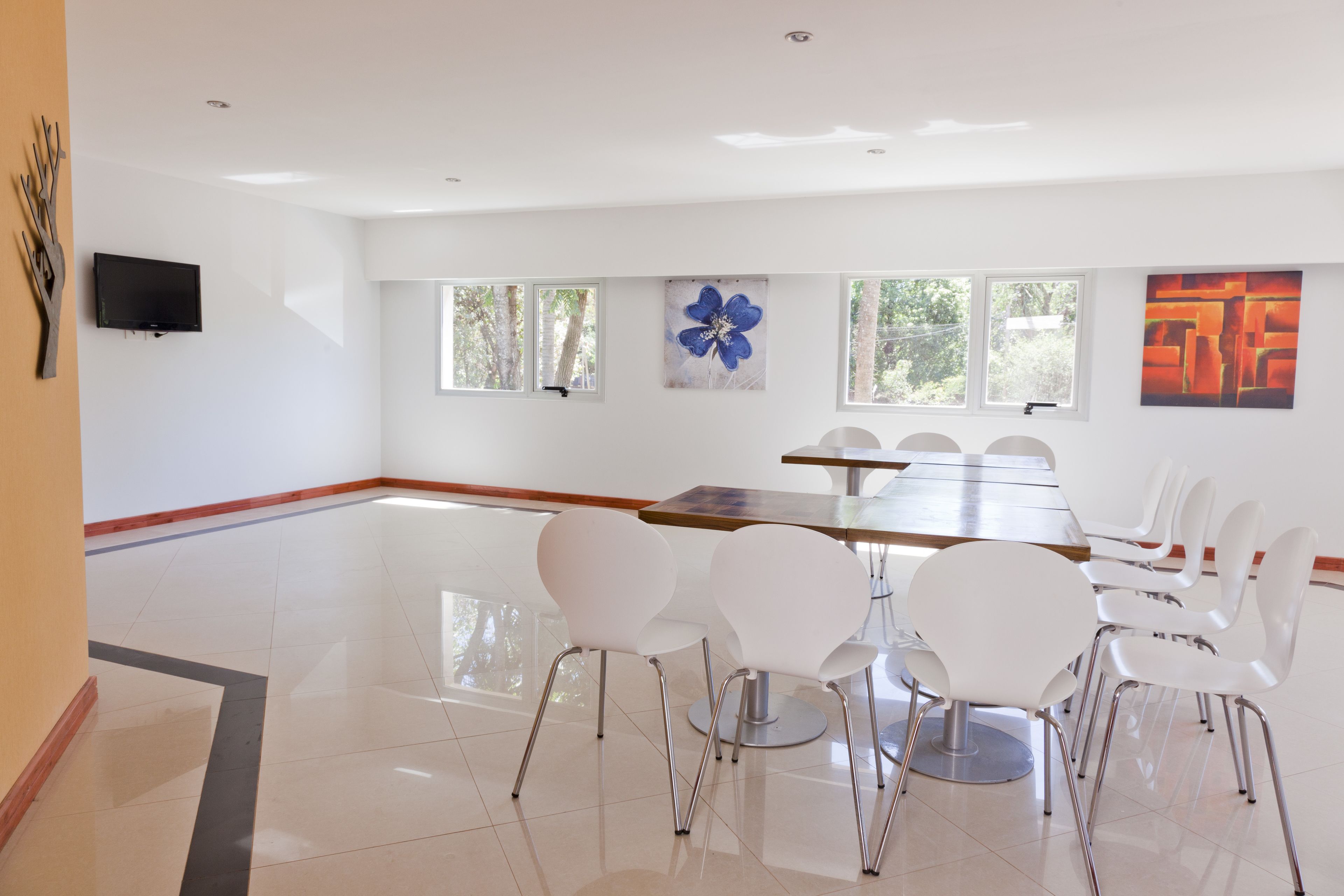 Una habitación amplia con una larga mesa y sillas blancas, ventanas grandes y obras de arte en las paredes.