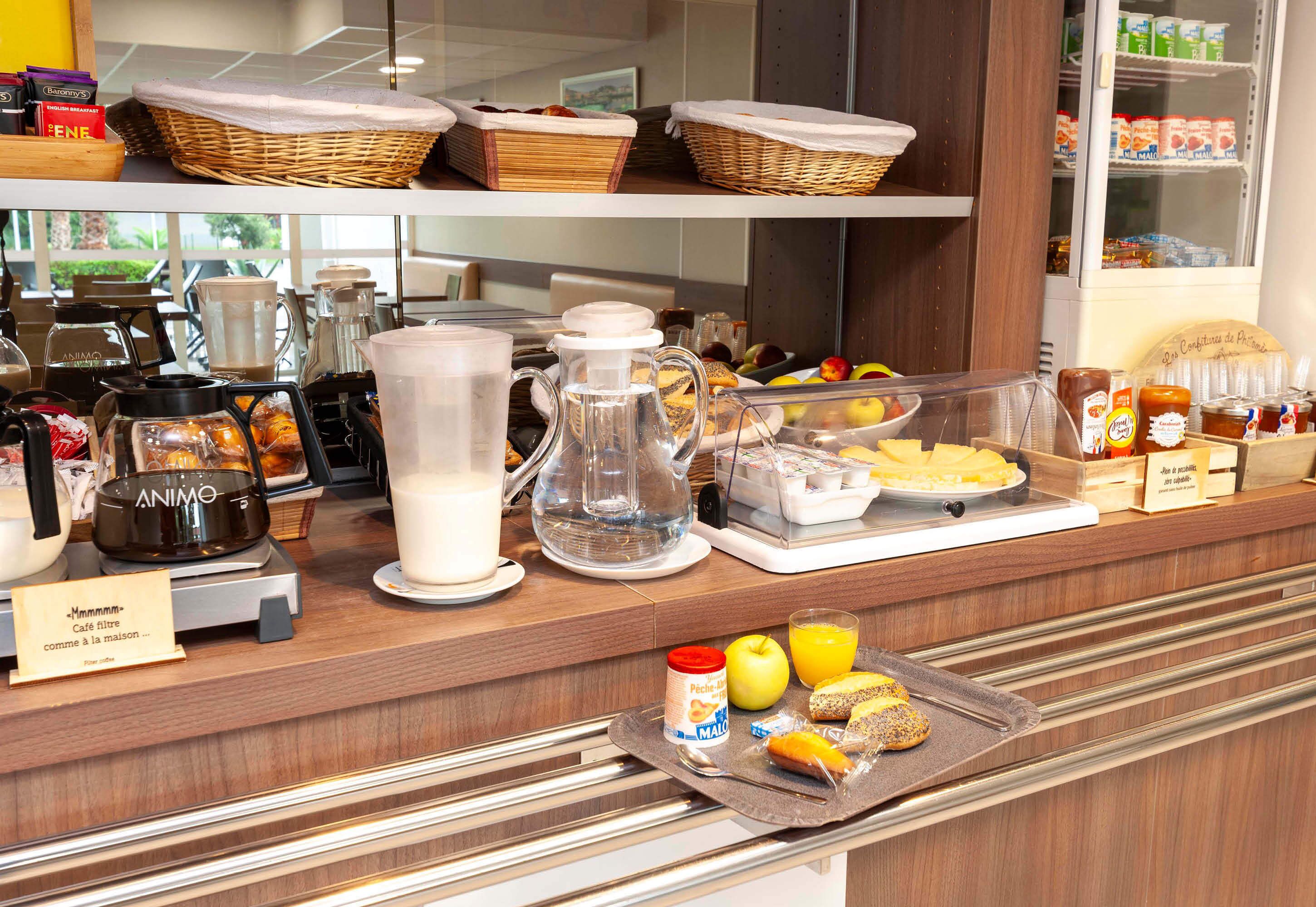 A breakfast buffet with various food items, a coffee machine, and a refrigerator in the background.