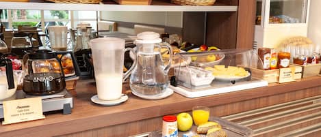 A breakfast buffet with various food items, a coffee machine, and a refrigerator in the background.