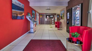 A hotel lobby with a red wall, a reception desk, a vending machine, and red seating. - B&B HOTEL Saint-Jean de Luz (Saint-Jean-de-Luz)