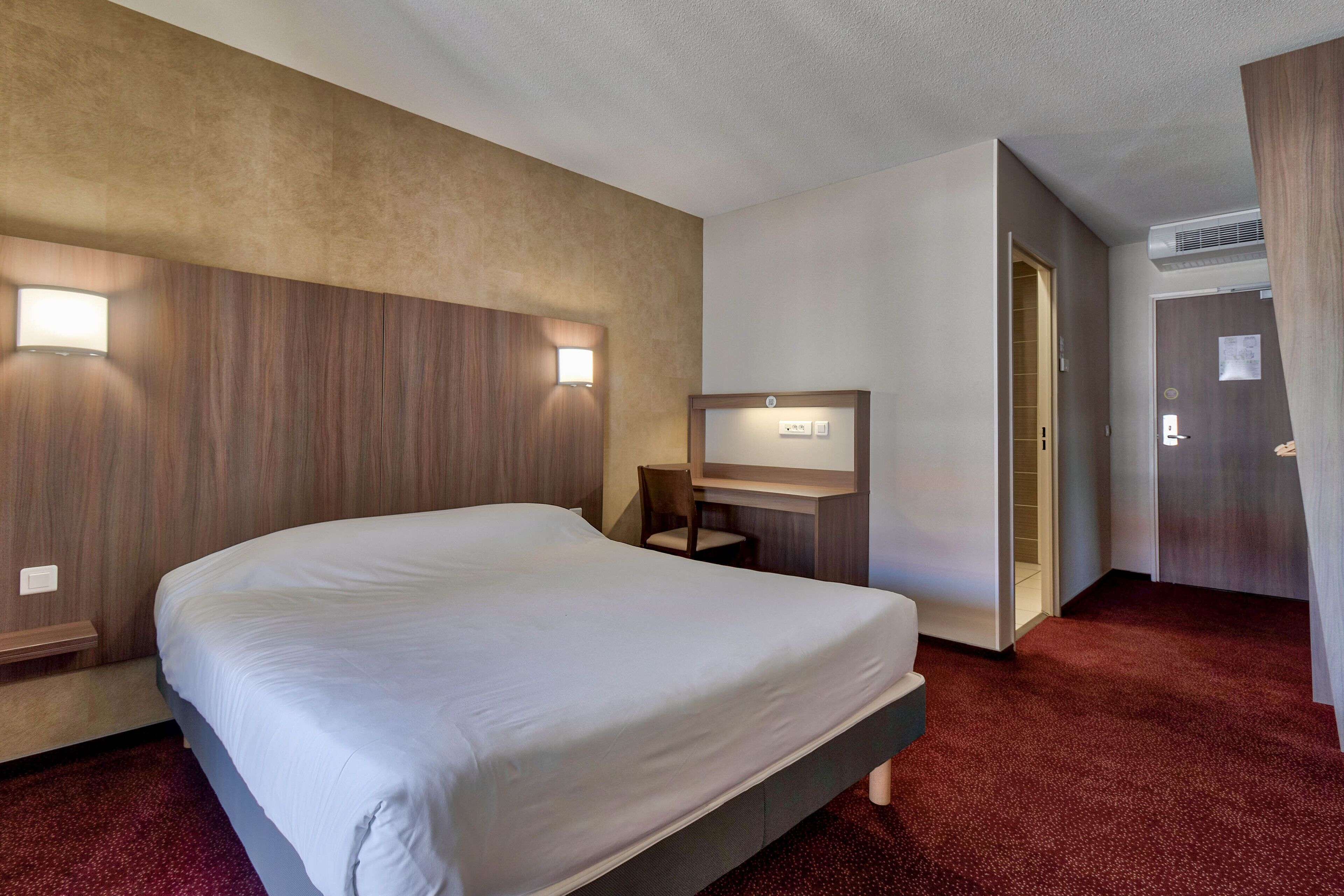 Una habitación de hotel con una cama grande, un escritorio con una silla, un espejo y un armario.