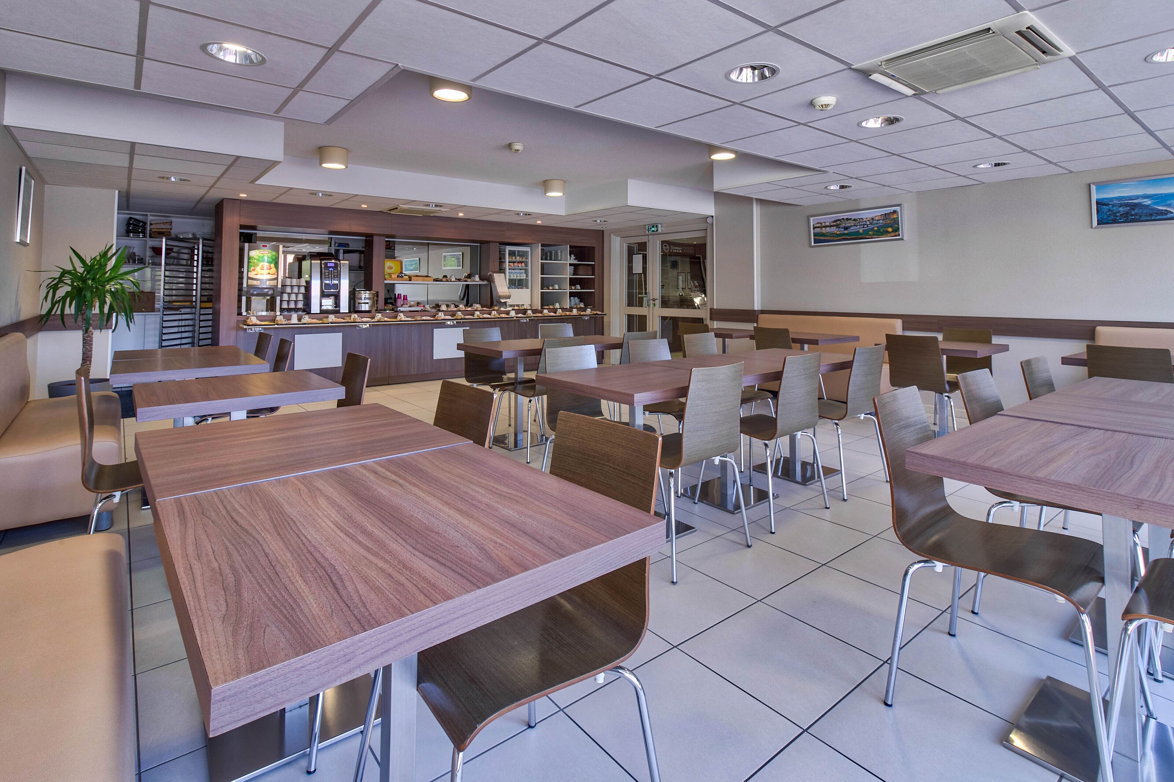 Una cafetería moderna con varias mesas y sillas, una barra con alimentos y una escalera que sube a un nivel superior.