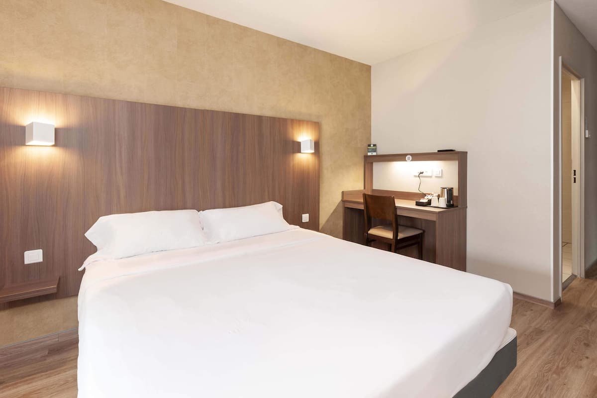 Ett hotellrum med en stor säng, ett skrivbord med en stol och två väggmonterade lampor.