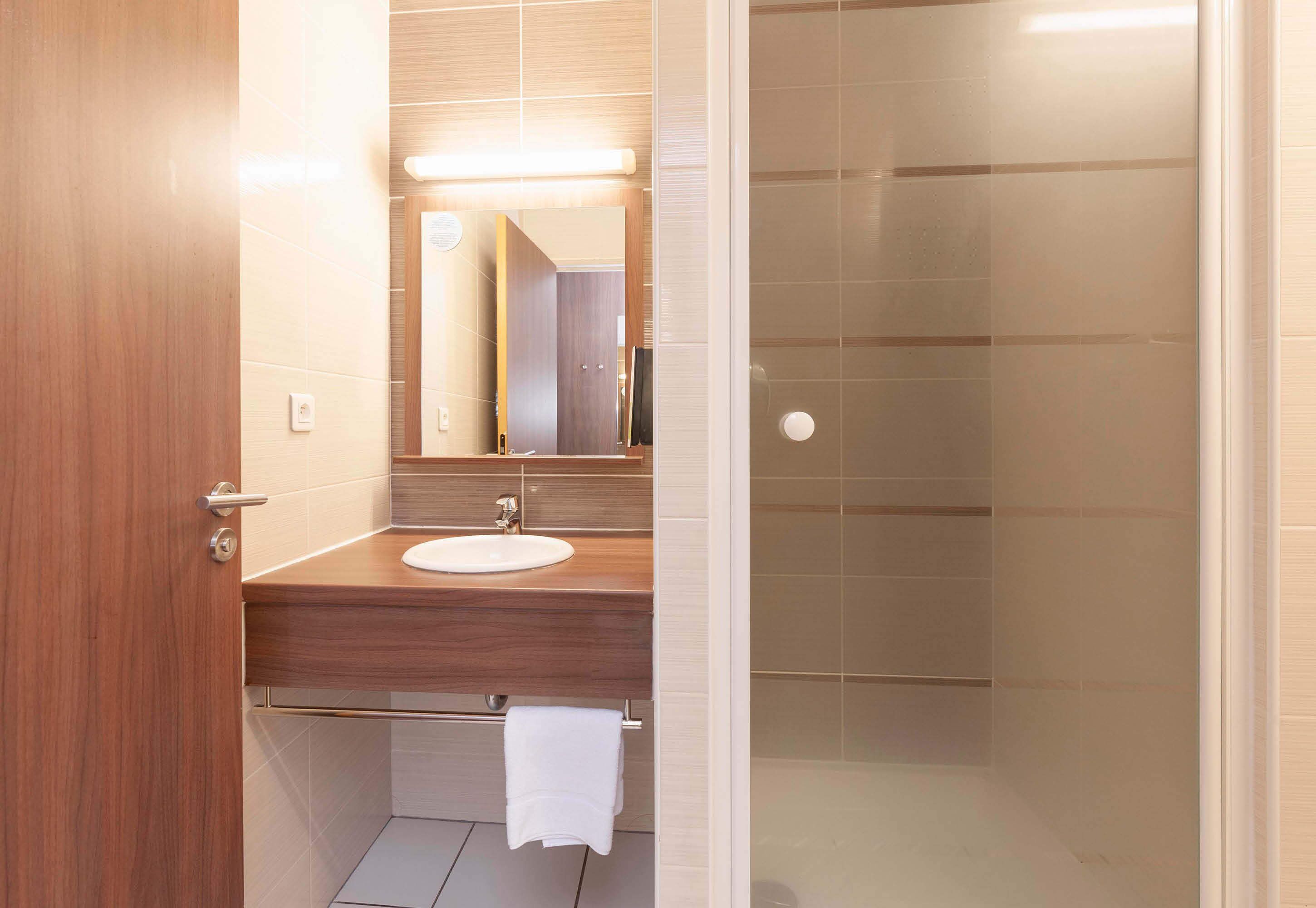 A modern bathroom with a wooden vanity, a white sink, and a glass shower enclosure.