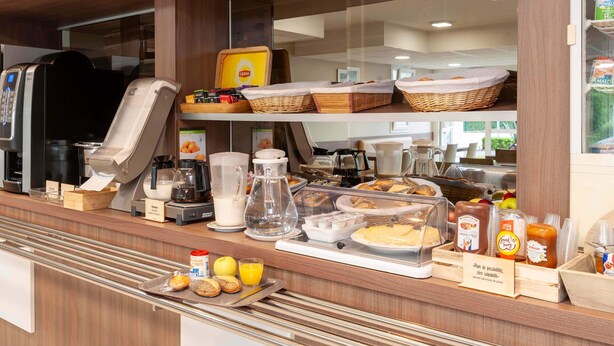 A breakfast buffet with various food items, a coffee machine, and a juice dispenser. - B&B HOTEL Saint-Jean de Luz (Saint-Jean-de-Luz)