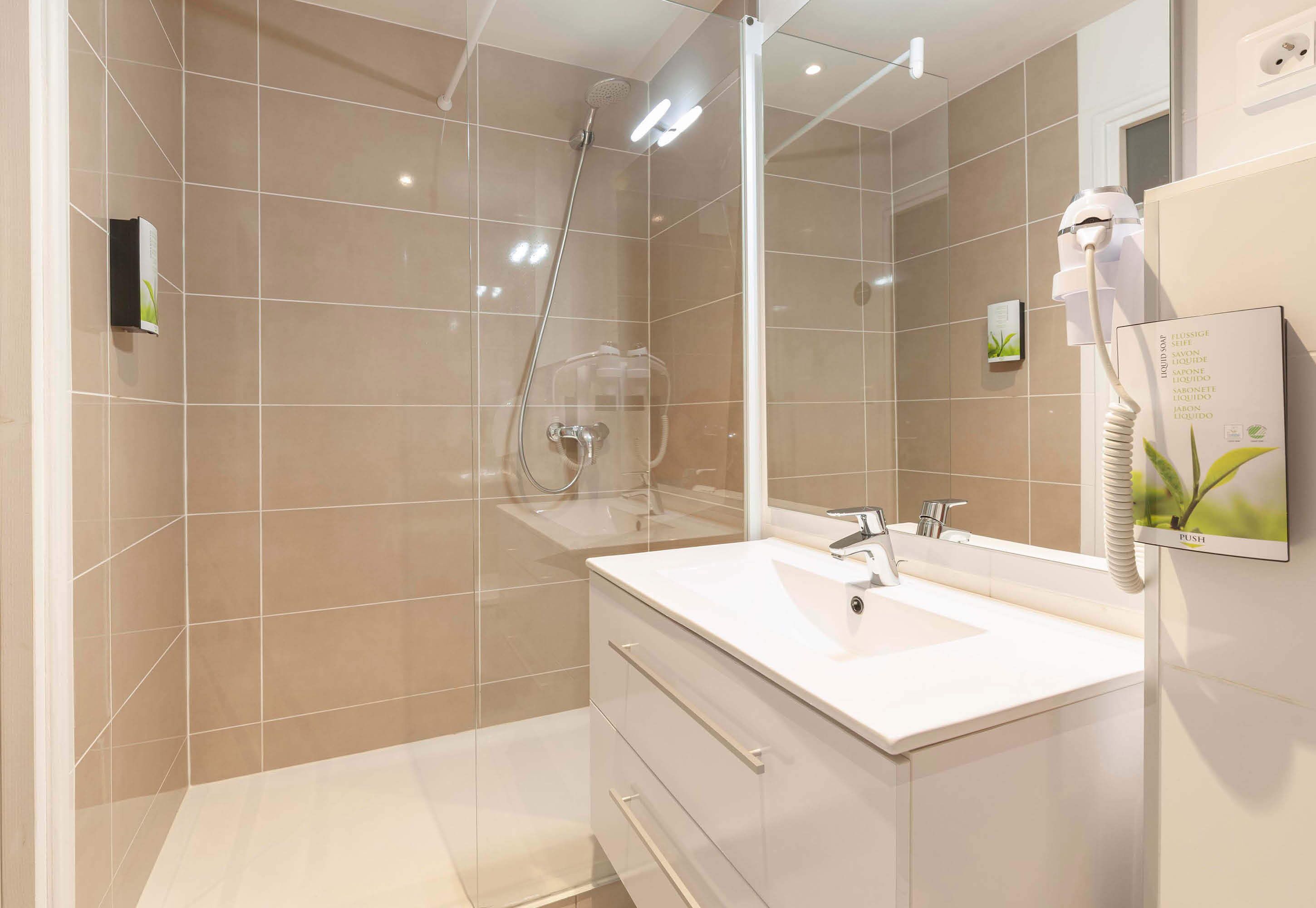 Een moderne badkamer met een glazen douchecabine, een witte wastafel met spiegel en een haardroger aan de muur.