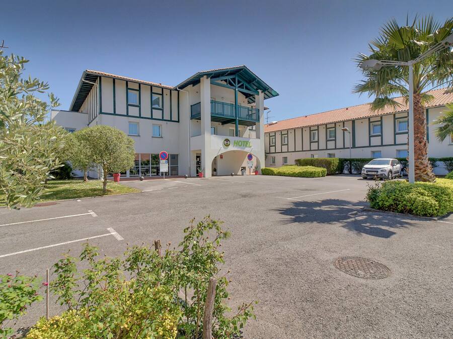 Un hotel de diseño moderno, con una entrada destacada, un balcón y un estacionamiento con algunos coches.