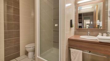 Un baño moderno con ducha envuelta en vidrio, inodoro y tocador con lavamanos y espejo.
