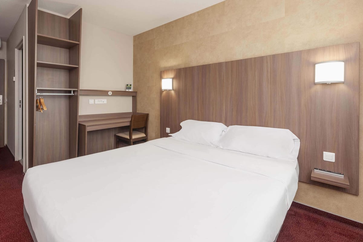 Ett hotellrum med en stor säng, ett skrivbord med en stol och en garderob med plats för att hänga kläder.