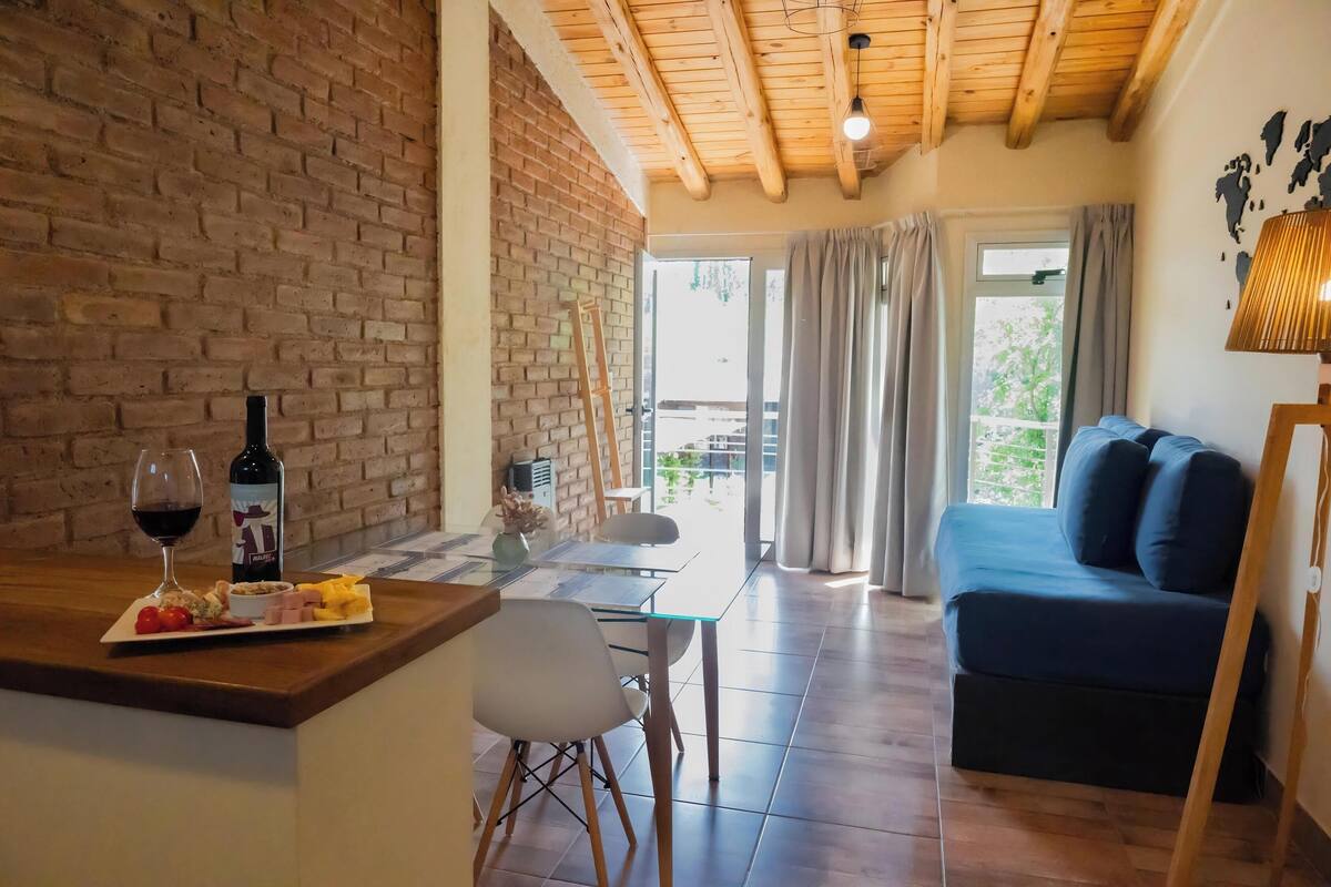 Une pièce chaleureuse avec un mur en briques, un plafond en bois, une table à manger avec des chaises, un canapé et une vue sur l’extérieur.