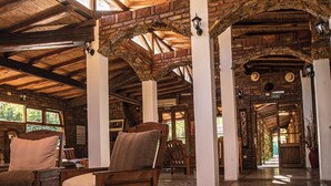 Un hall d’entrée spacieux avec des poutres et des colonnes en bois, un comptoir d’accueil et des espaces détente.