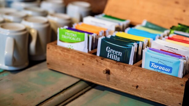 Eine Holzkiste mit Packungen, darunter die Markennamen 'Green Hills' und 'Taragui', auf einer Holzunterlage.