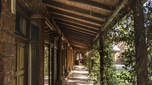 Un couloir couvert aux murs de pierre et aux poutres en bois, menant à l’entrée d’un bâtiment.
