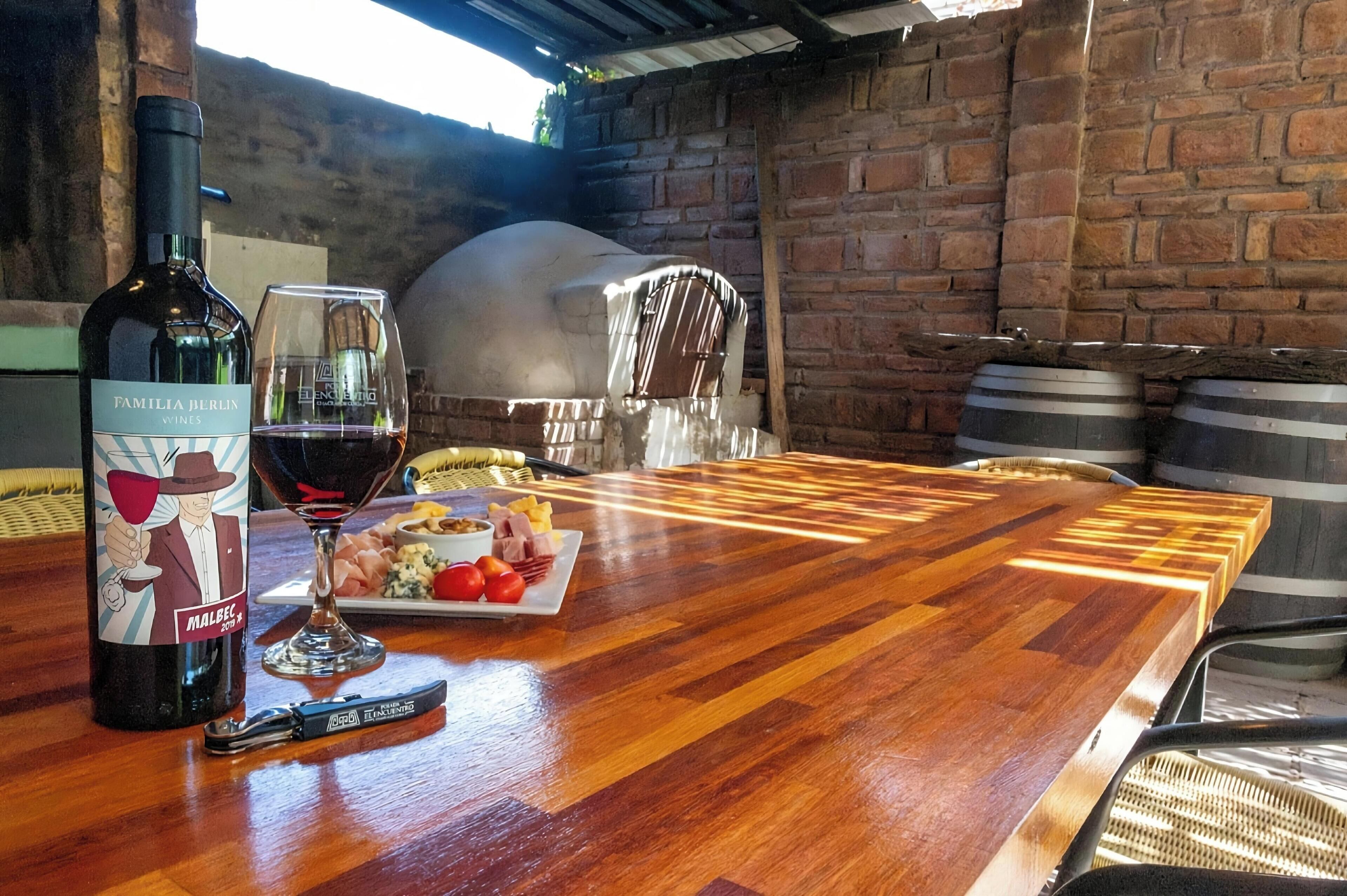 Un tavolo di legno con una bottiglia di vino, un bicchiere e un piatto di cibo.