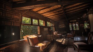 Un intérieur rustique avec des poutres en bois, des murs en briques et de grandes fenêtres donnant sur un paysage verdoyant.