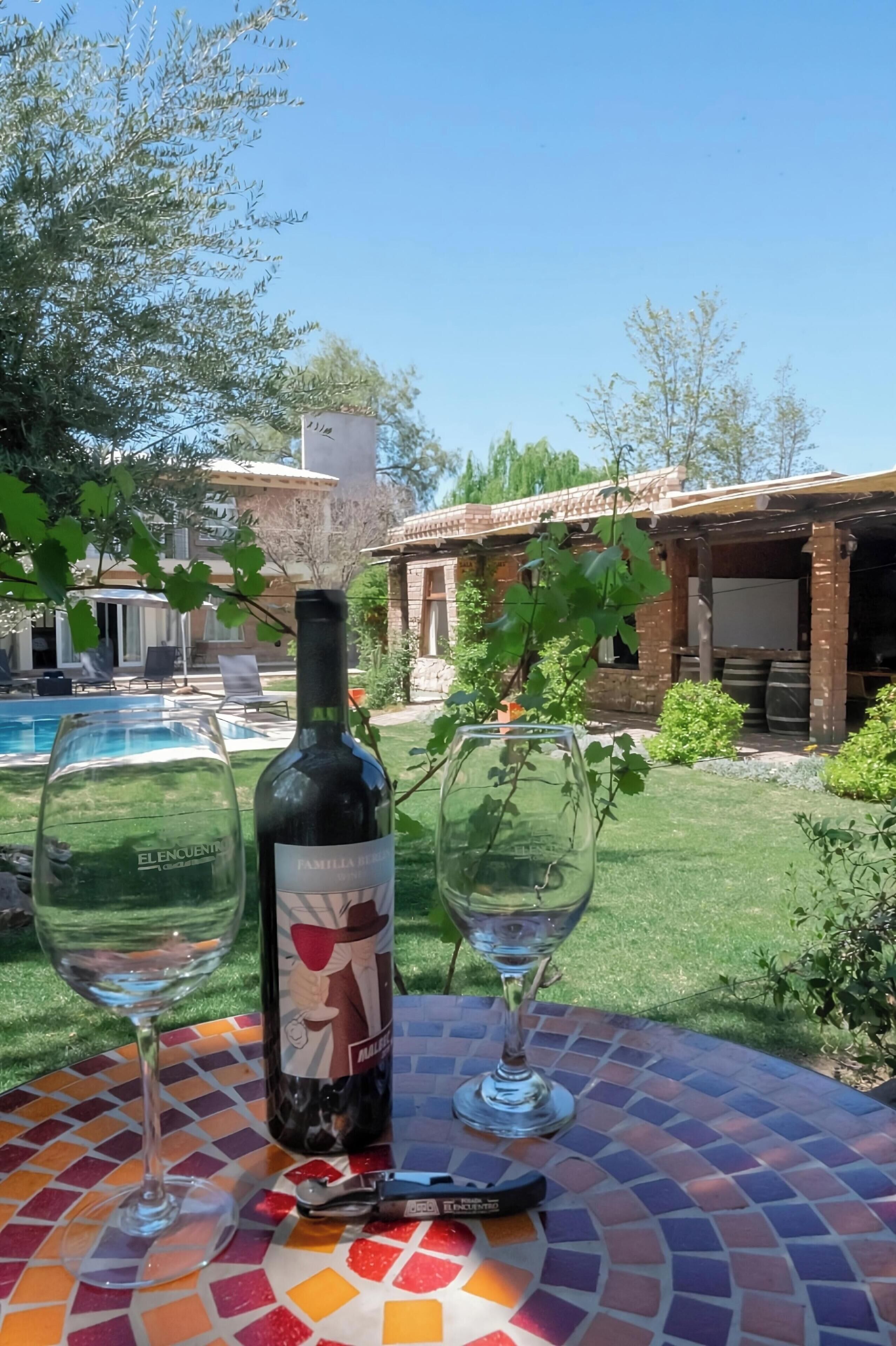 A patio with a mosaic table, a wine bottle, and two wine glasses.