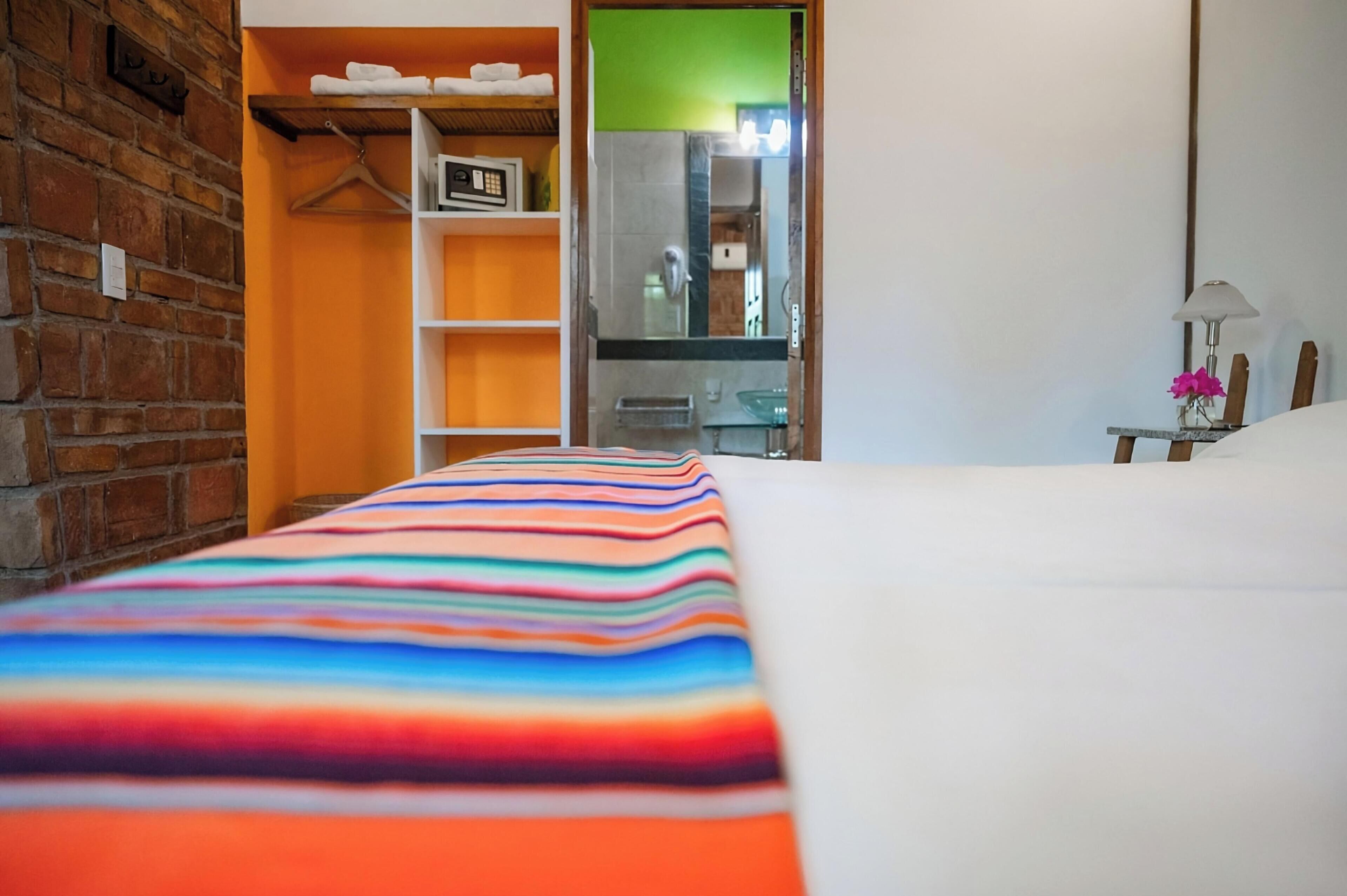 Una camera d'albergo con un letto, un muro in mattoni, un armadio in legno e un bagno parzialmente visibile attraverso una porta aperta.