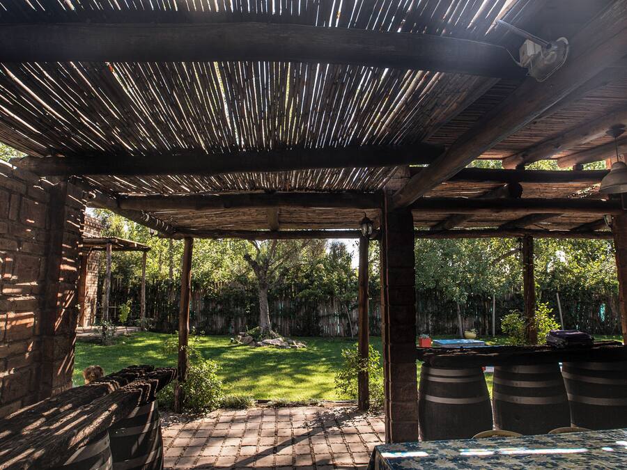 A covered outdoor seating area with a brick wall, wooden beams, and a view of a grassy yard.
