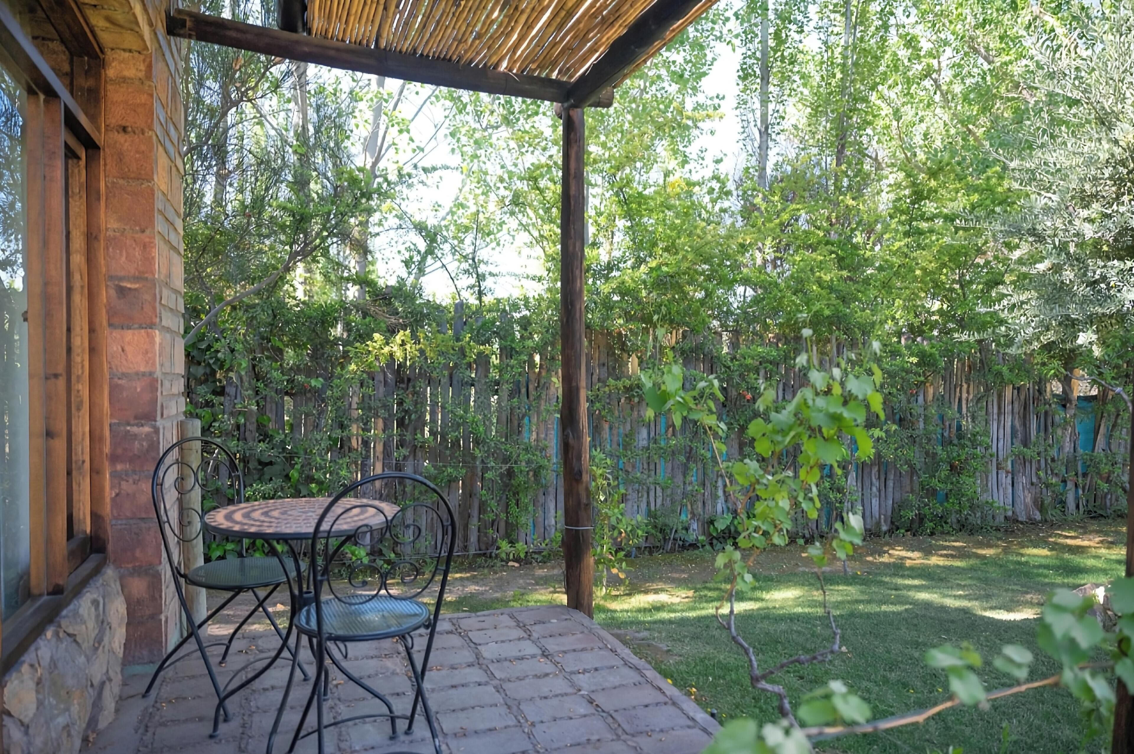 A patio with a table and chairs, a wooden pergola, and a wooden fence in a garden setting.