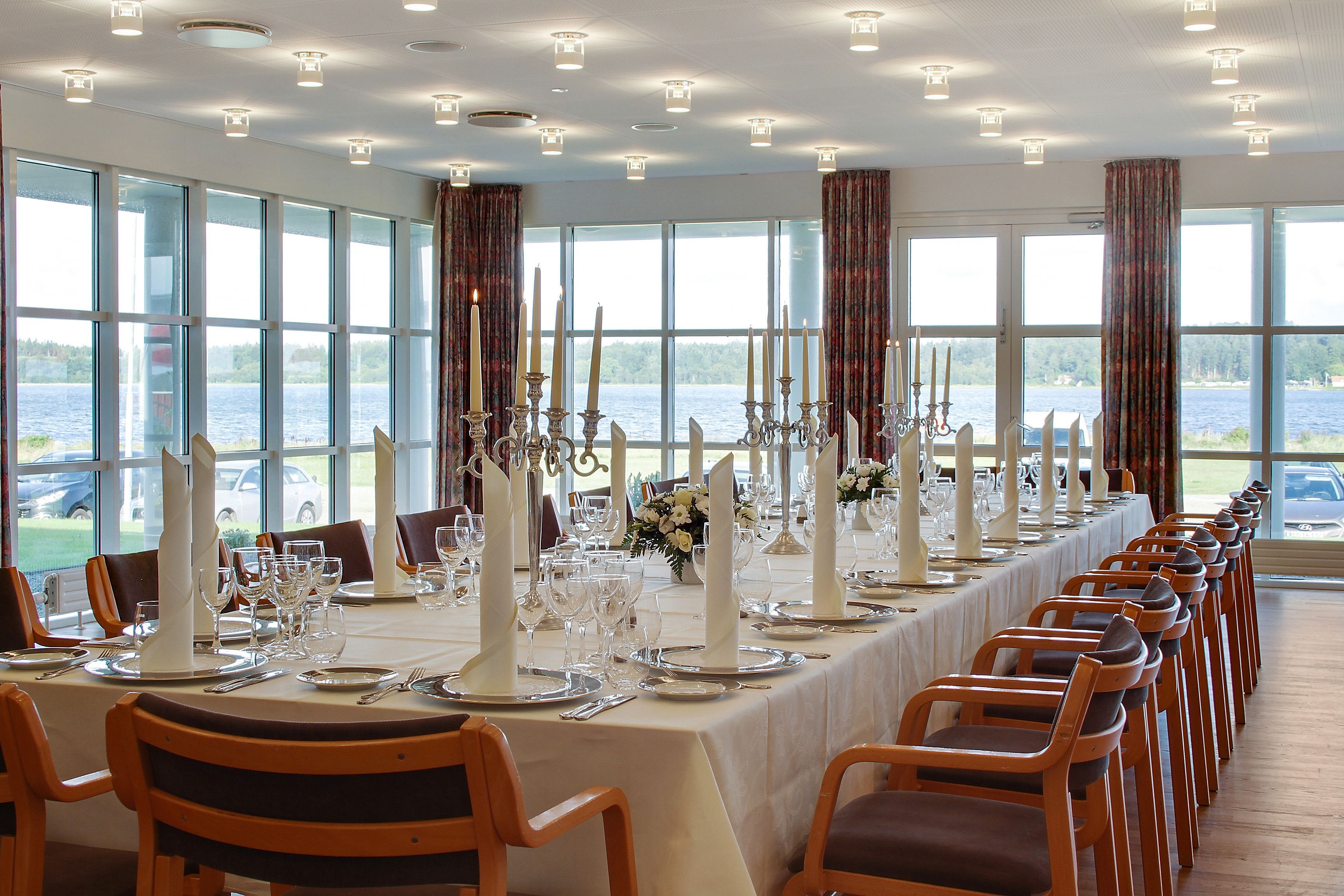 Una larga mesa de comedor dispuesta para un evento formal, con velas, copas y vistas al lago.