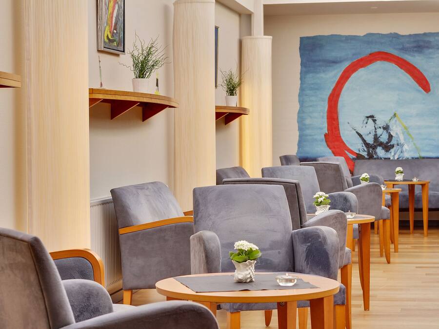 A modern lounge area with grey upholstered chairs, wooden tables, and potted plants.