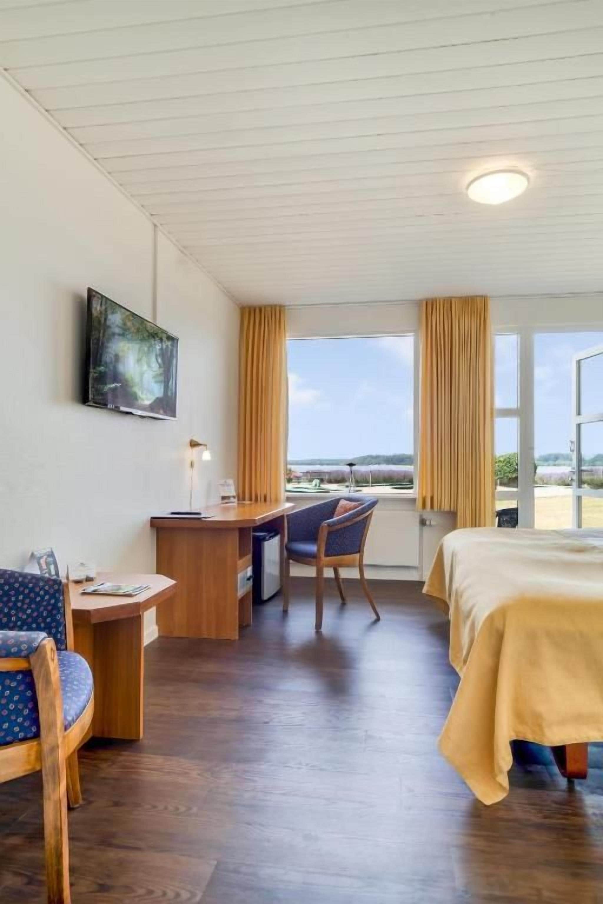 Una habitación de hotel con una cama, un escritorio, una silla y un ventanal con cortinas.