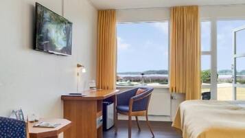 Una habitación de hotel con una cama, un escritorio, una silla y un ventanal con cortinas.