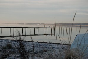 A wooden pier extending into a calm body of water, surrounded by frosty vegetation. - Hotel Pinenhus (Roslev)