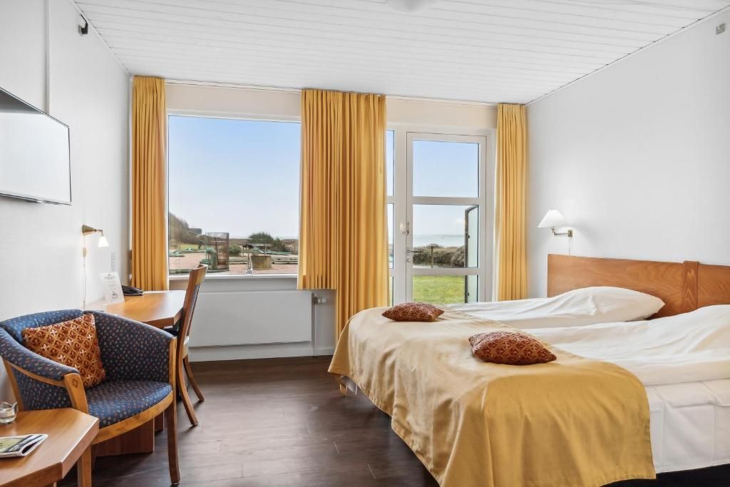 Habitación de hotel con una cama, un escritorio con silla, una ventana con cortinas y vistas al exterior.