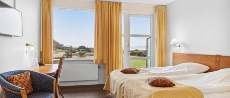 Une chambre d’hôtel avec un lit, un bureau et une chaise, une fenêtre avec des rideaux et une vue sur l’extérieur.