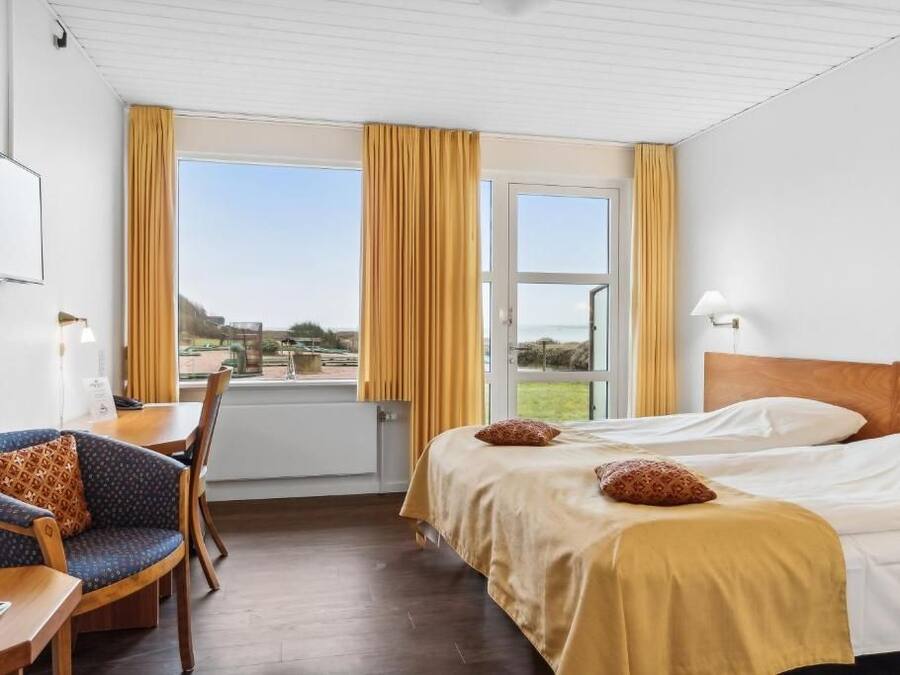 Habitación de hotel con una cama, un escritorio con silla, una ventana con cortinas y vistas al exterior.