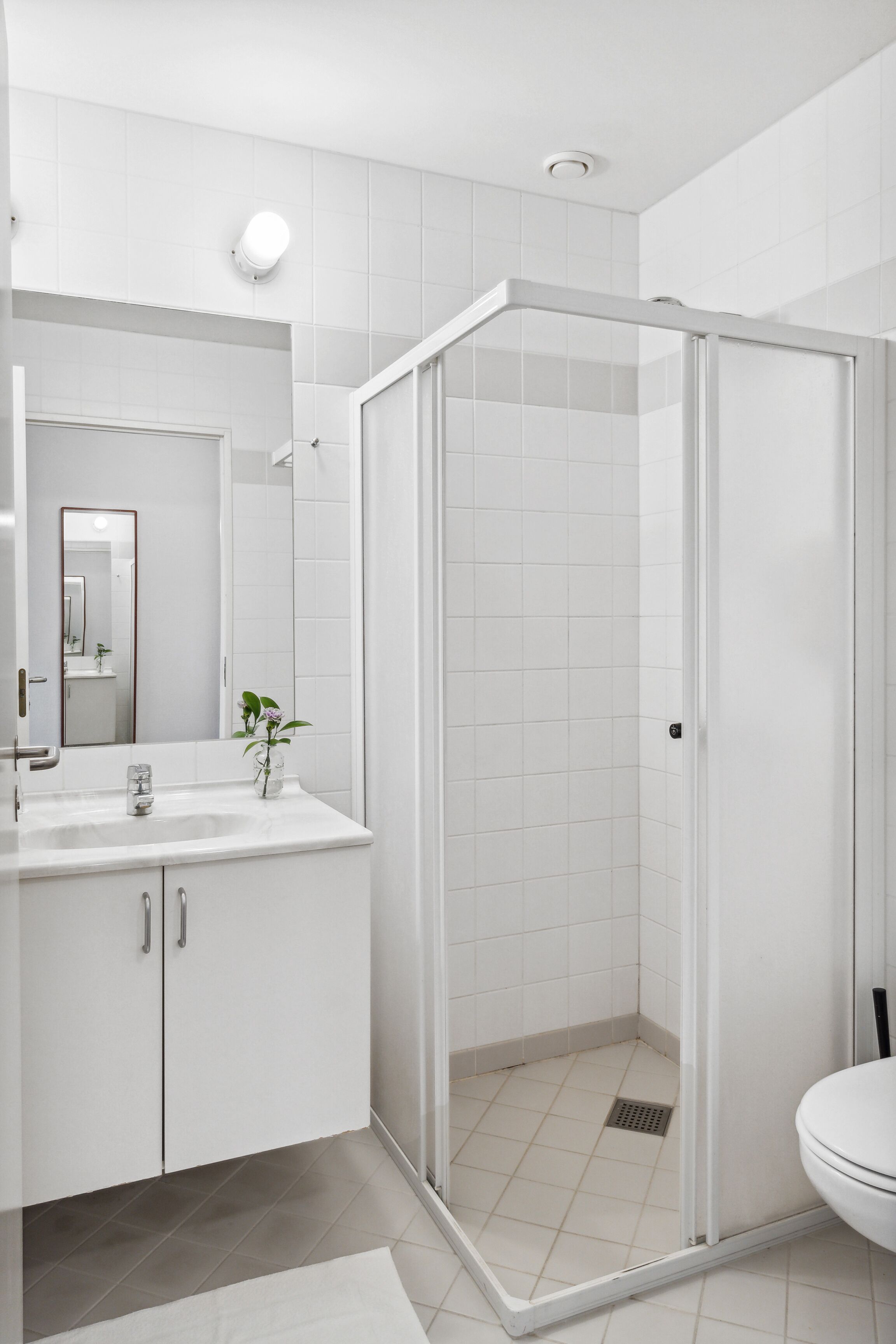 A modern bathroom with a glass-enclosed shower, white tiles, a sink with a mirror, and a toilet.