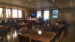 A restaurant with wooden tables and chairs, a TV screen, and a bar area.