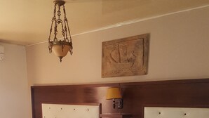 Habitación de hotel con dos camas, cabecera de madera, mesita de noche con lámpara y alfombra roja estampada.