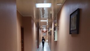 Un largo pasillo estrecho con suelo de baldosas blancas y paredes color beige.