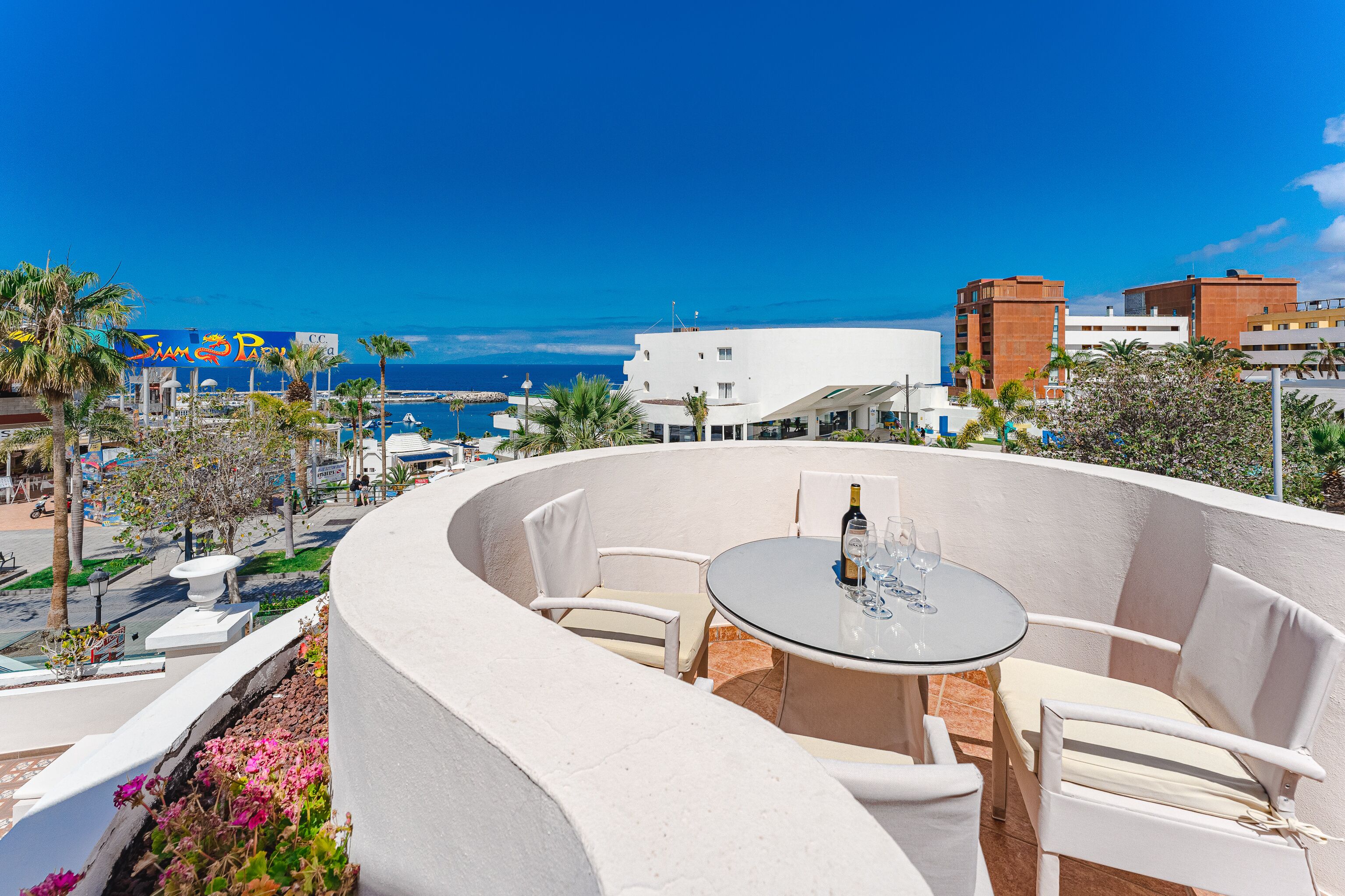 A curved outdoor seating area with a table and chairs, overlooking a beach and cityscape.