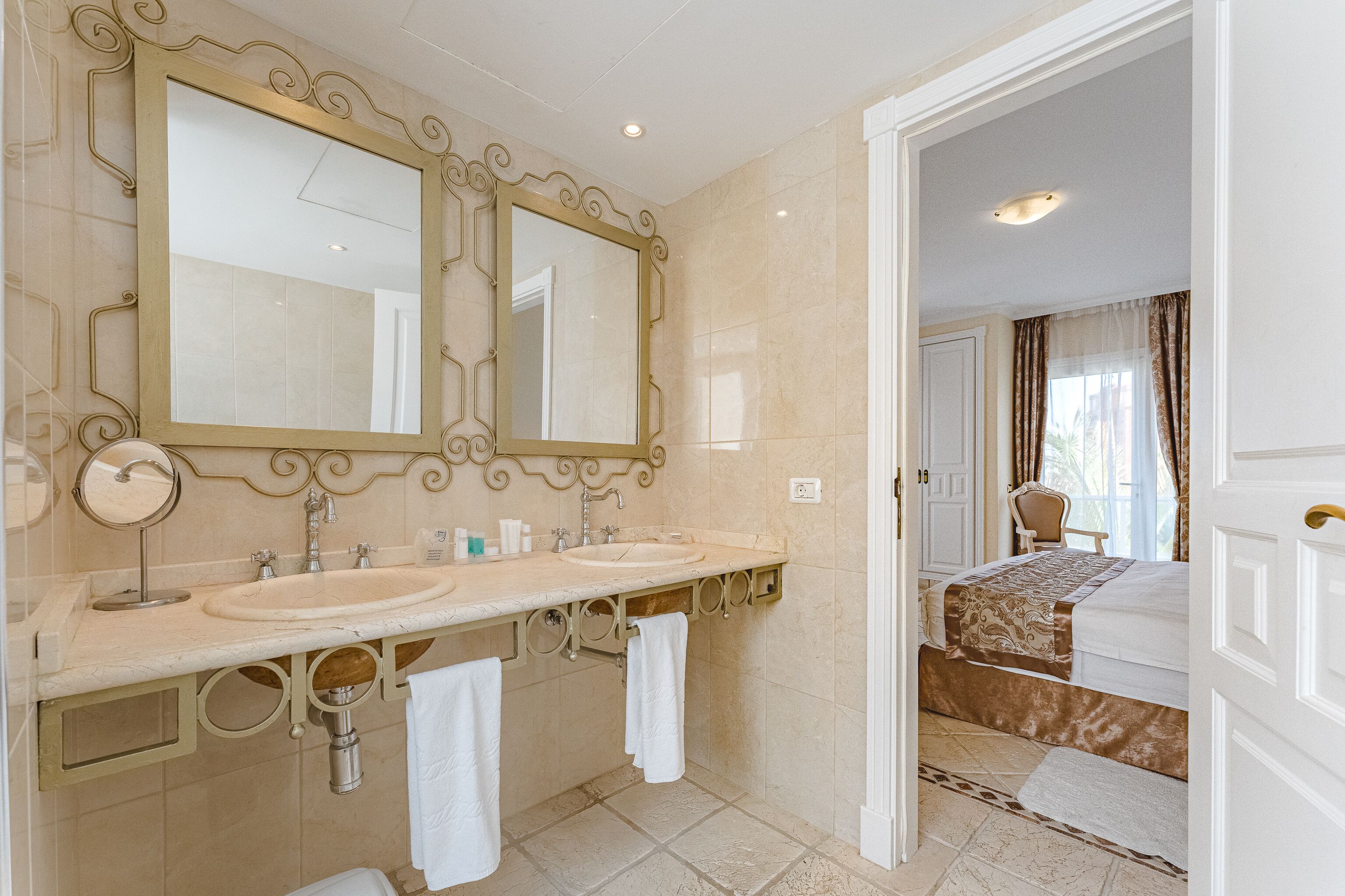 A bathroom with two sinks, a large mirror, and a door leading to a bedroom.