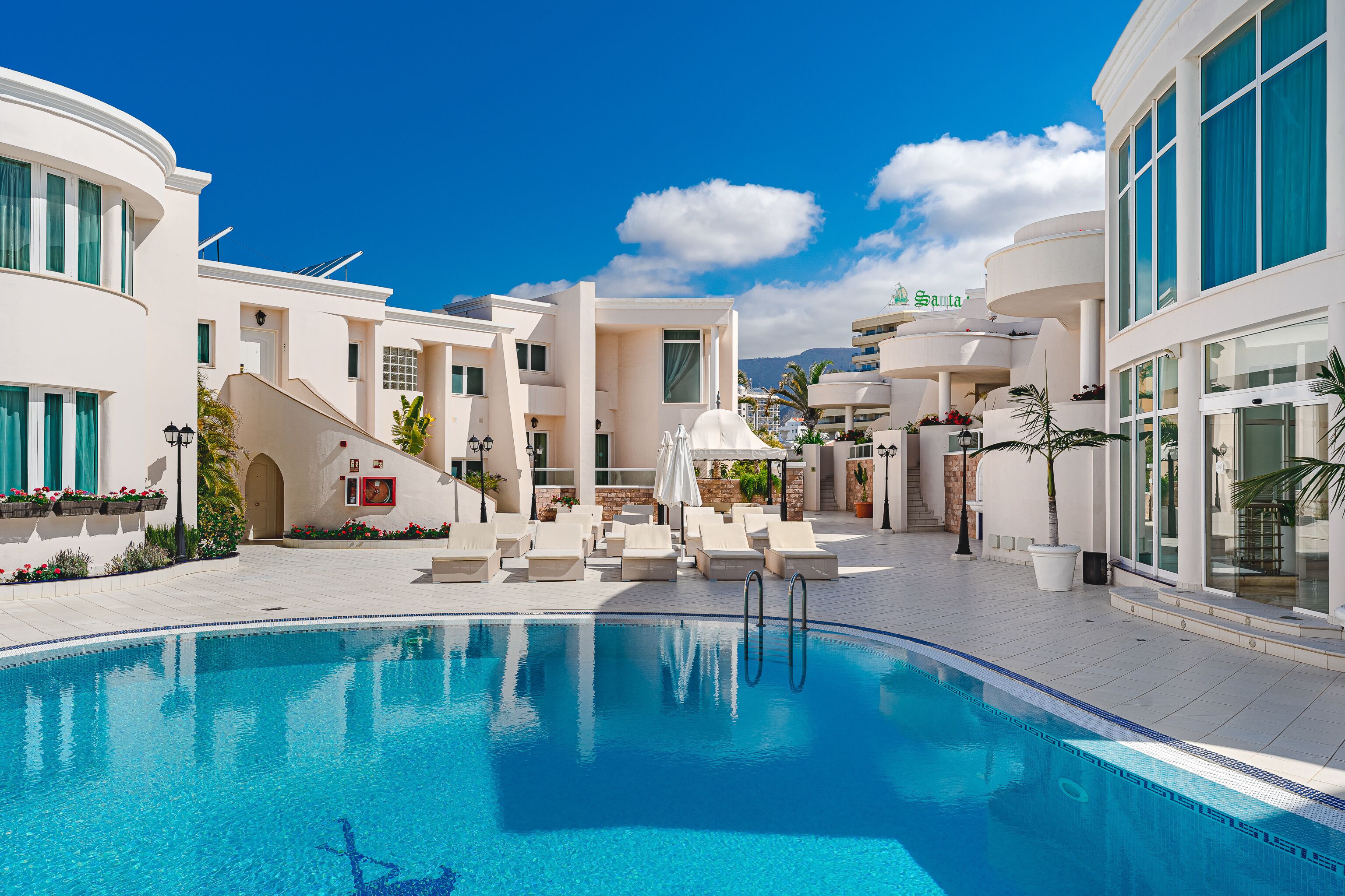 A modern hotel with a swimming pool, multiple lounge areas, and a view of the mountains.