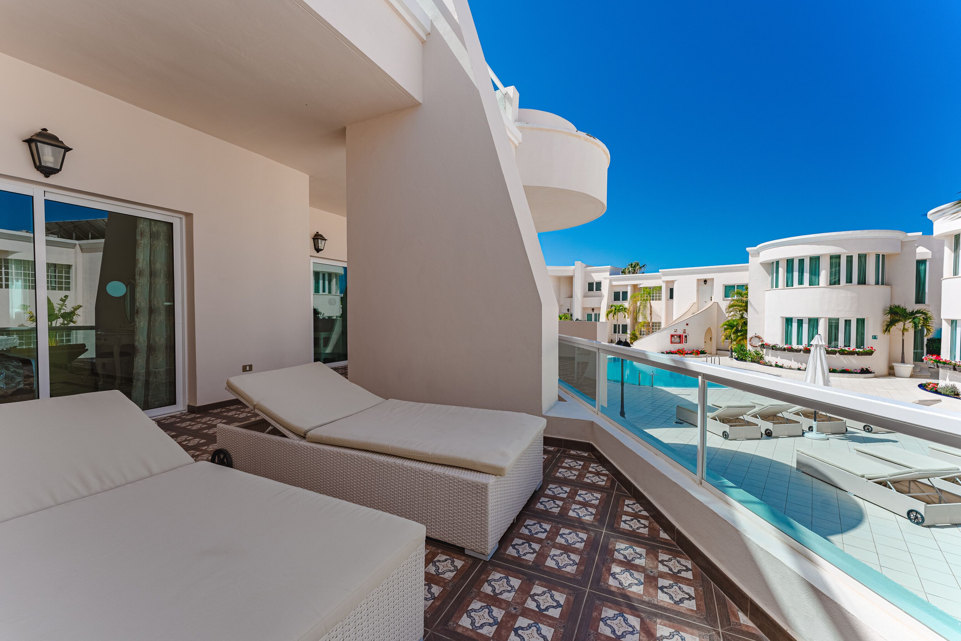 Ein moderner Hotelbalkon mit Liegestühlen, einem Pool und wolkenlosem, blauem Himmel.