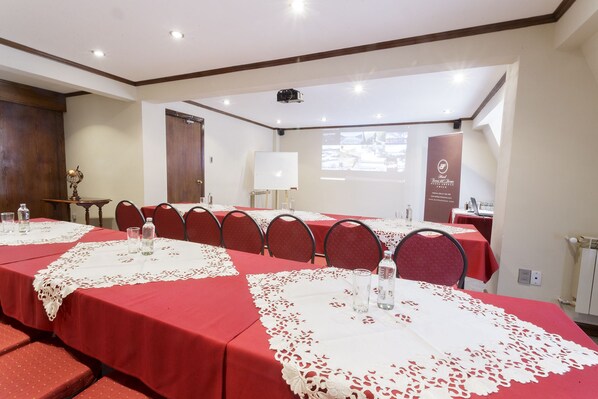 A conference room with long tables, red tablecloths, and white lace doilies. There are chairs around the tables, a projector screen, and a whiteboard.